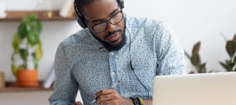 Man writing in notebook at computer